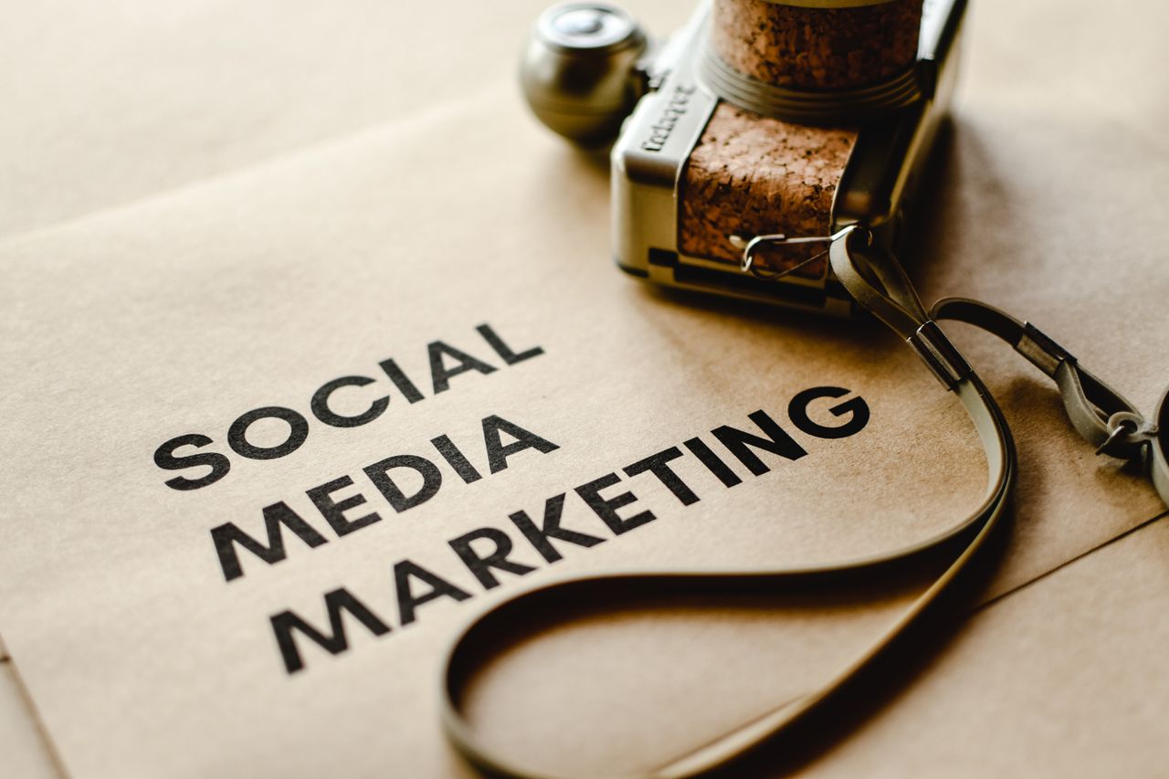 Vue rapprochée d’un appareil photo posé sur du papier brun, avec le texte Social Media Marketing, mettant en avant les thématiques du marketing numérique.